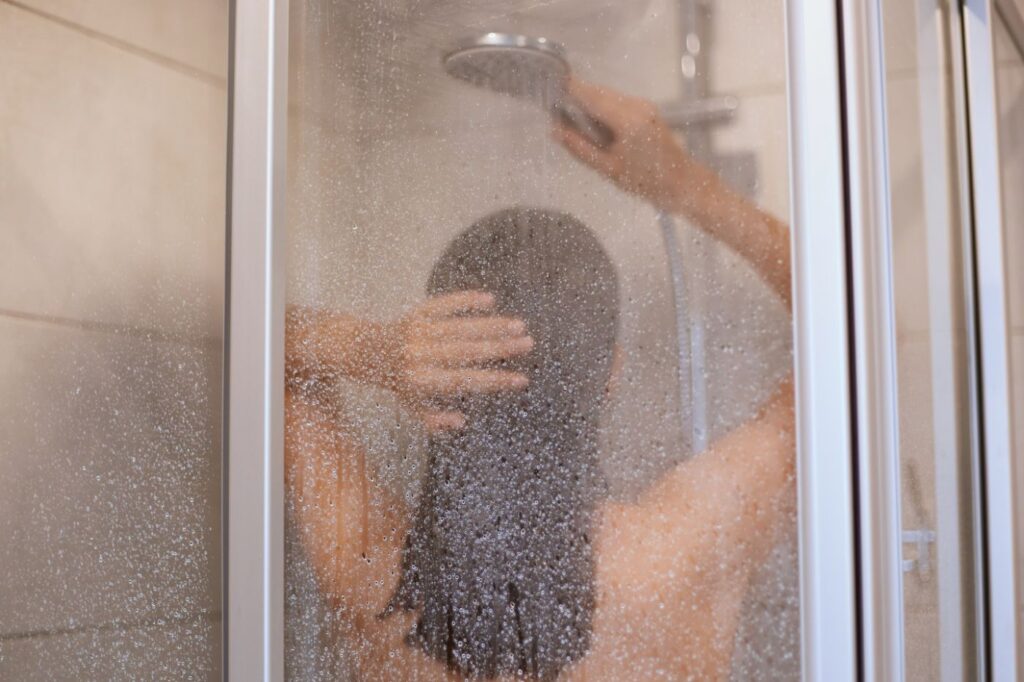 back view of beautiful young slim shirtless woman taking shower
